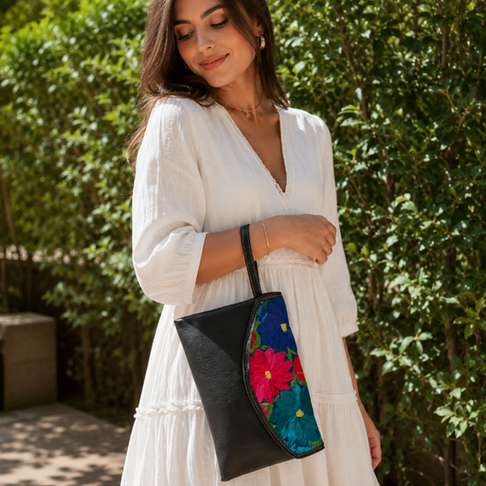 Woman wearing a black leather shoulder bag with colorful floral embroidered flap outdoors