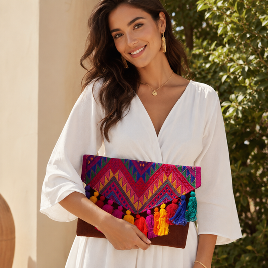 Woman holding a colorful tribal embroidered clutch with multicolor tassels and suede leather base outdoors