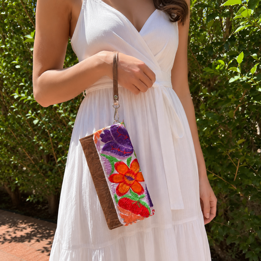 Woman holding a handmade leather clutch with vibrant colorful floral embroidery and wrist strap outdoors
