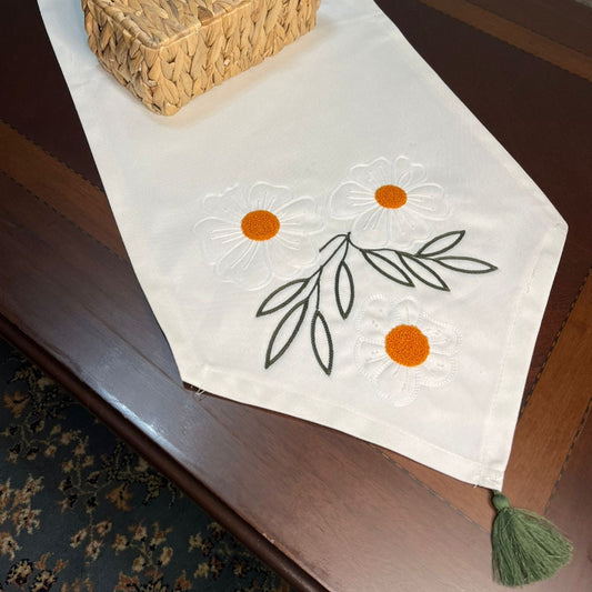 White cotton table runner with embroidered daisy flowers and orange centers on wooden coffee table