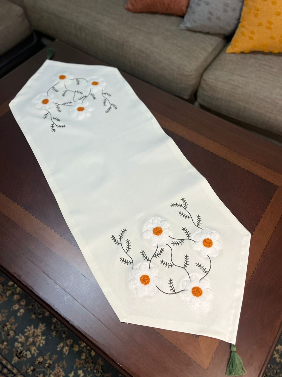 White hand embroidered floral table runner with orange flower details on wooden coffee table
