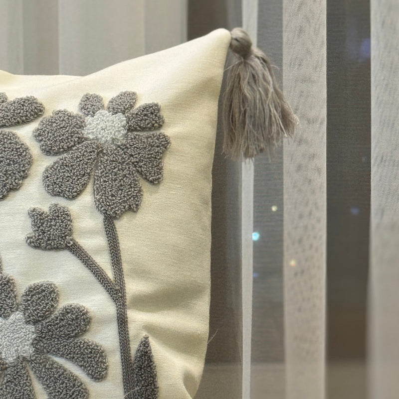 Rectangular cream cushion cover with grey tufted floral embroidery and tassels on each corner