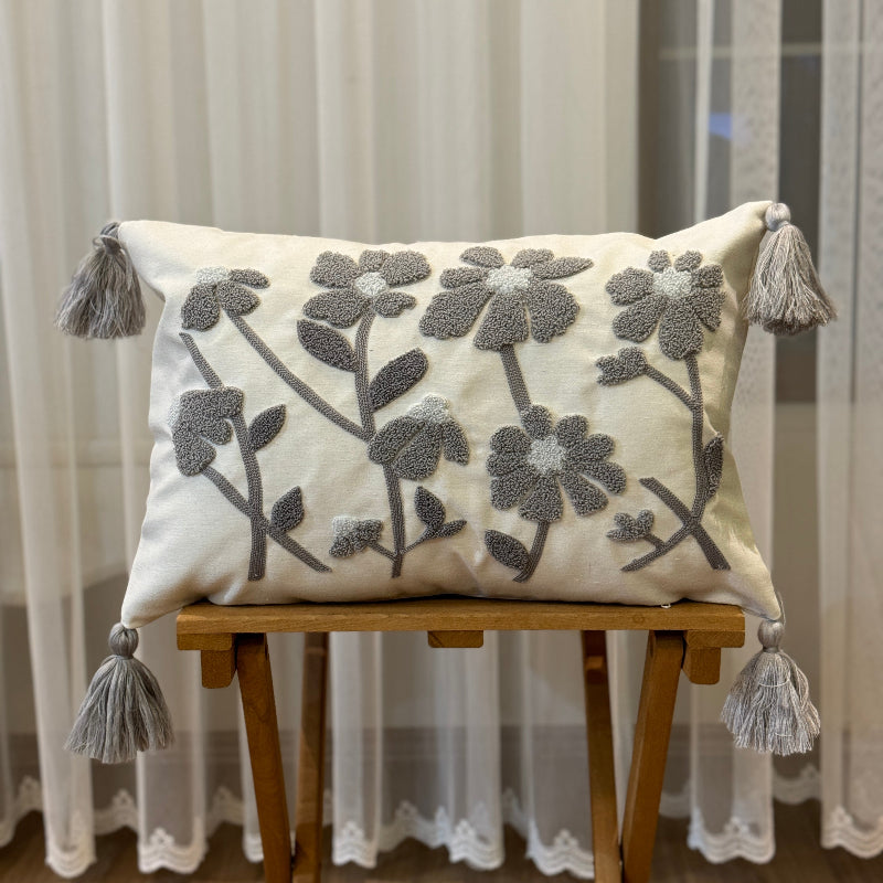 Rectangular cream cushion cover with grey tufted floral embroidery and tassels on each corner