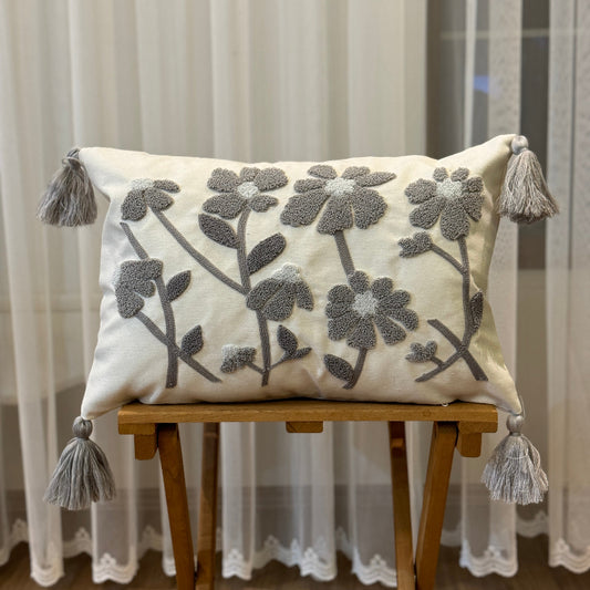 Rectangular cream cushion cover with grey tufted floral embroidery and tassels on each corner
