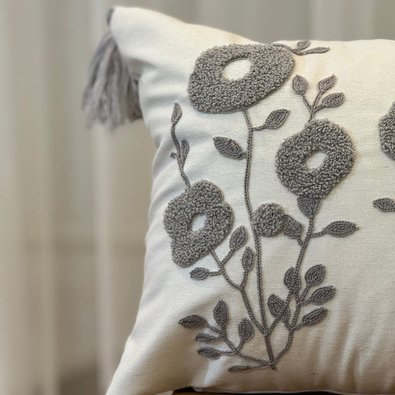 Rectangular cream cushion cover with grey tufted floral embroidery and tassels on each corner