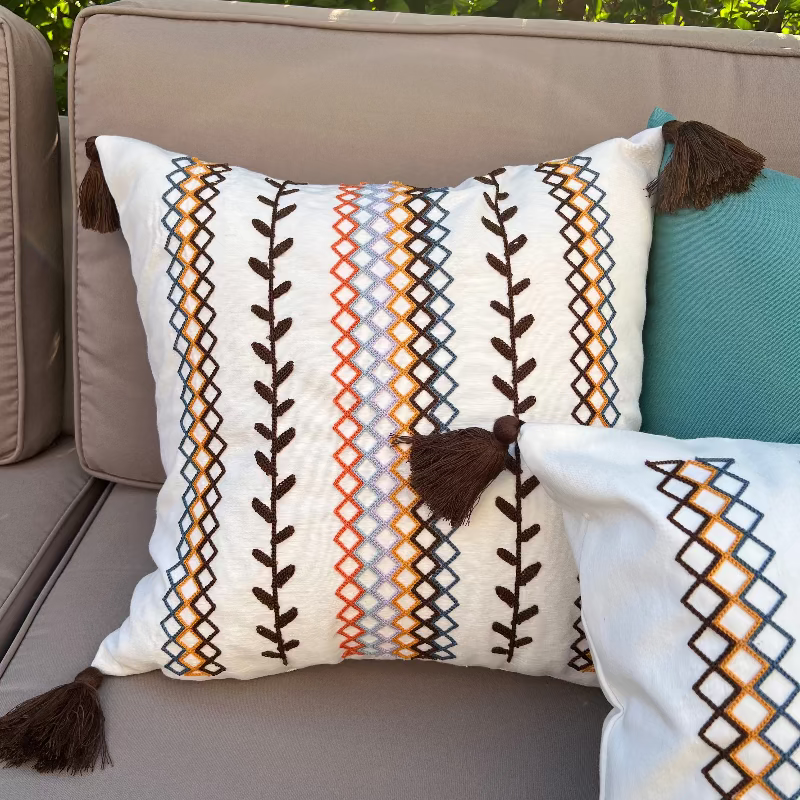 Square boho cushion cover with multi-color embroidered geometric and leaf pattern, finished with brown tassels on all four corners, 43x43 cm