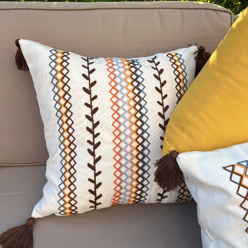 Square boho cushion cover with multi-color embroidered geometric and leaf pattern, finished with brown tassels on all four corners, 43x43 cm