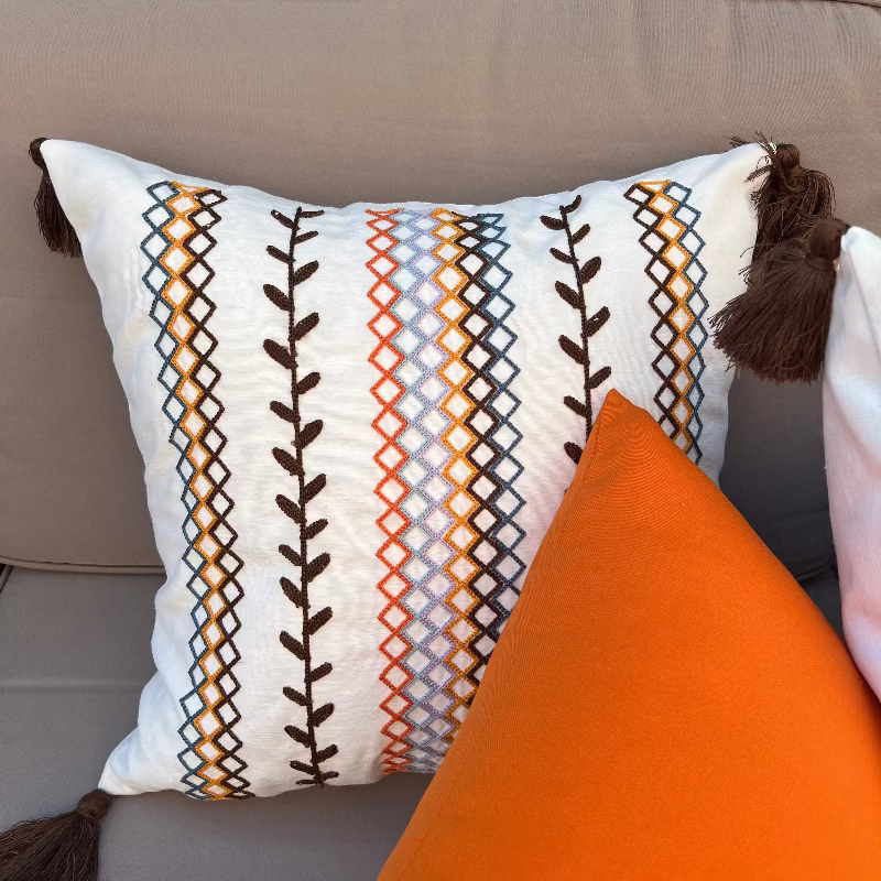 Square boho cushion cover with multi-color embroidered geometric and leaf pattern, finished with brown tassels on all four corners, 43x43 cm