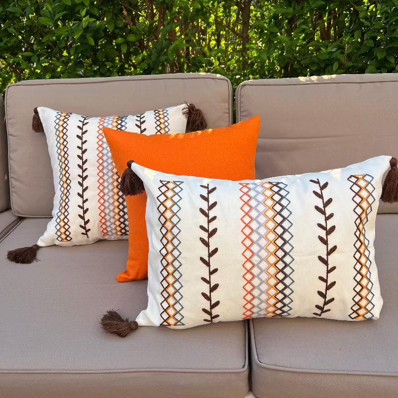 Square boho cushion cover with multi-color embroidered geometric and leaf pattern, finished with brown tassels on all four corners, 43x43 cm