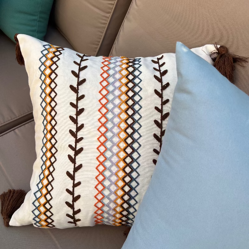 Square boho cushion cover with multi-color embroidered geometric and leaf pattern, finished with brown tassels on all four corners, 43x43 cm