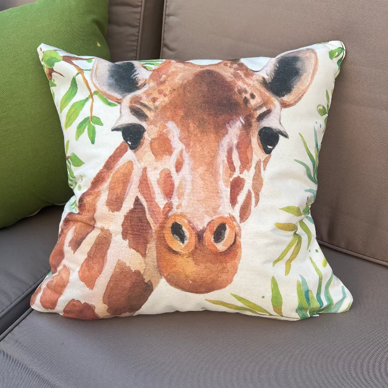 Watercolor giraffe cushion cover with botanical leaves on a decorative white pillow