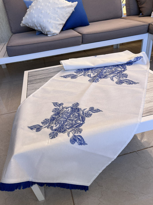 White table runner with blue floral print and blue fringe on a coffee table