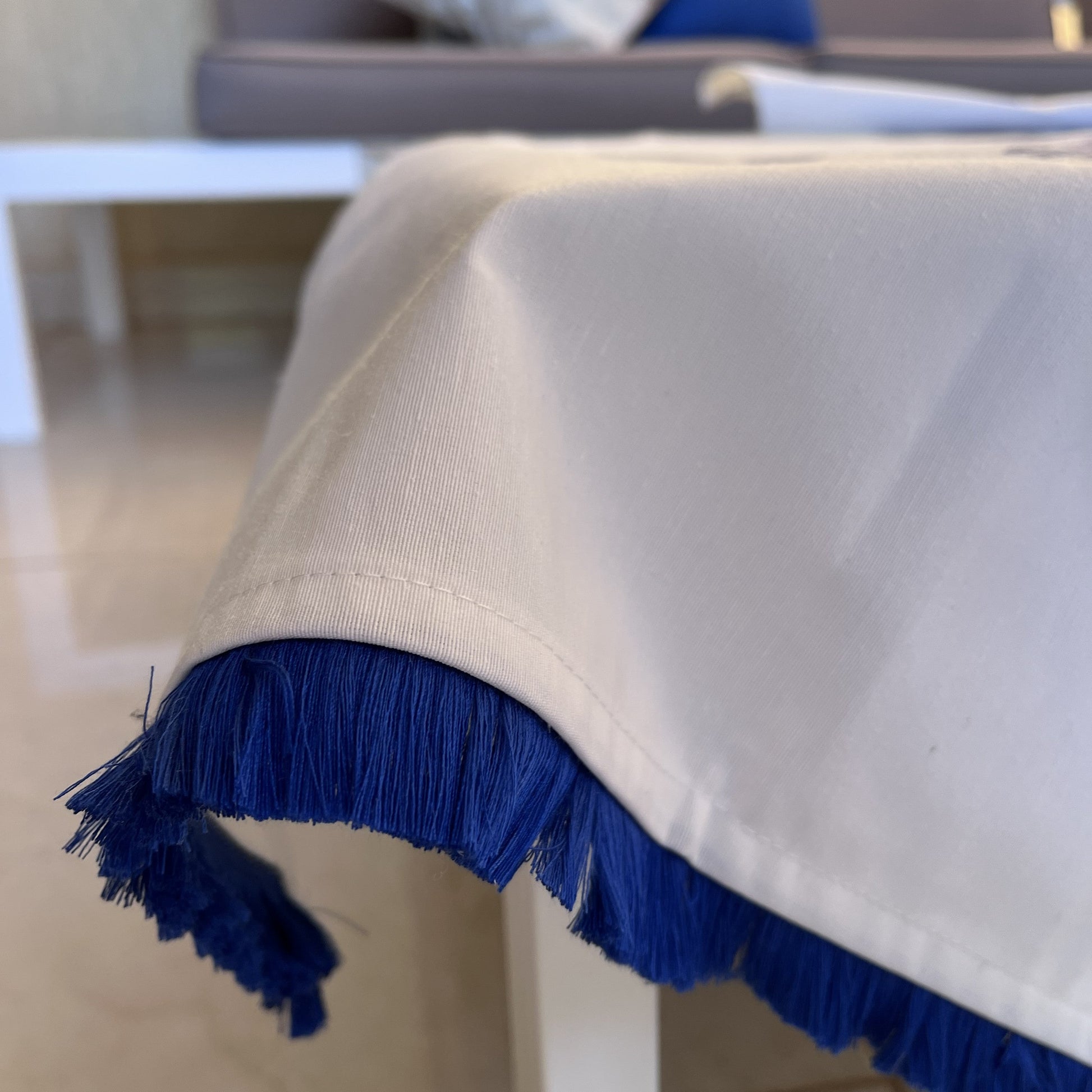 White table runner with blue floral print and blue fringe on a coffee table