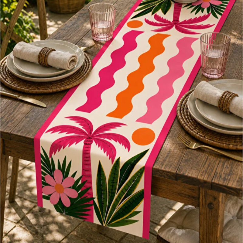 A tropical-themed table runner displayed on a rustic wooden dining table. The runner features a cream background with bold hot pink and orange wavy stripes, pink palm trees, green leaves, and a pink flower.