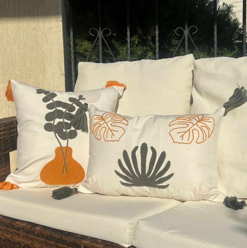 Embroidered boho cushion with vase and greenery design, cream fabric, and golden tassels on a wooden stool