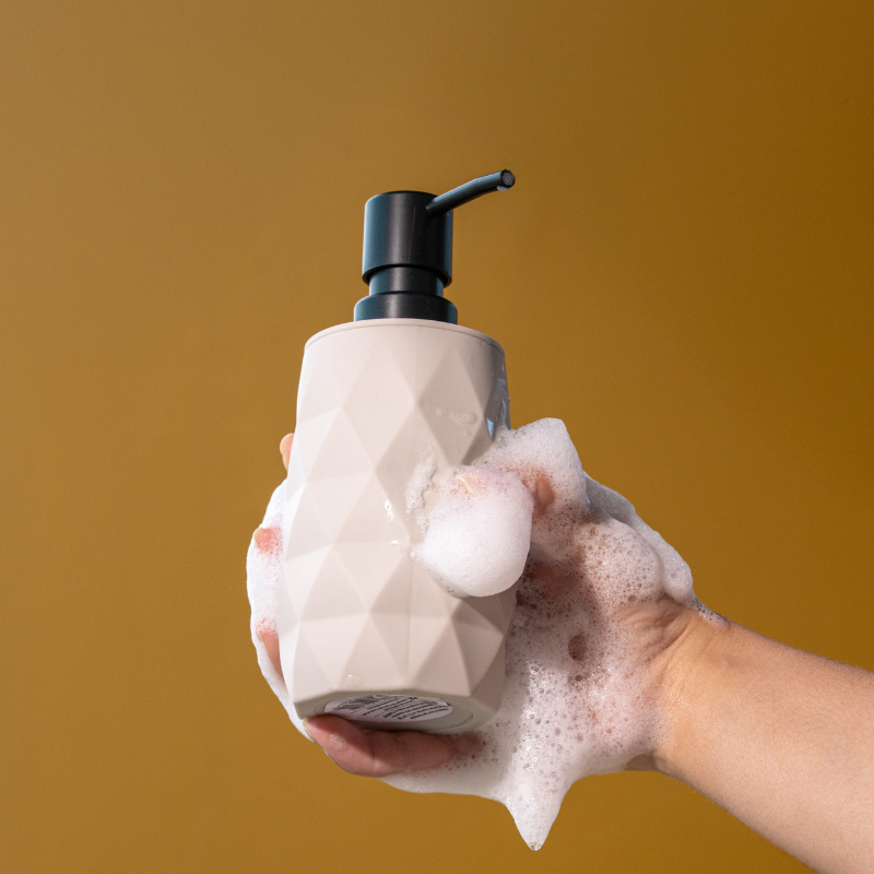 Set of four geometric soap dispensers in gray, white, beige, and black with bamboo detail