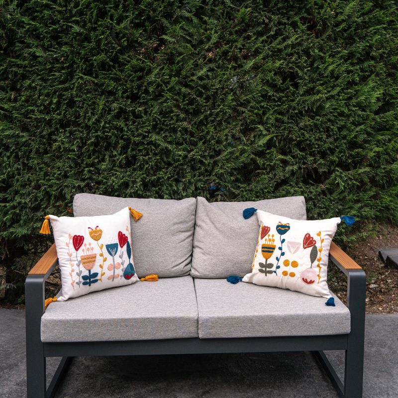 Boho embroidered floral cushion cover with colorful folk-inspired flowers and blue tassels on an ivory cotton base placed on outdoor grey sofa