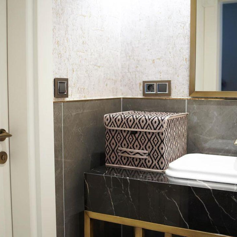 Beige and black diamond-patterned fabric storage box placed on a marble bathroom counter beside a sink.