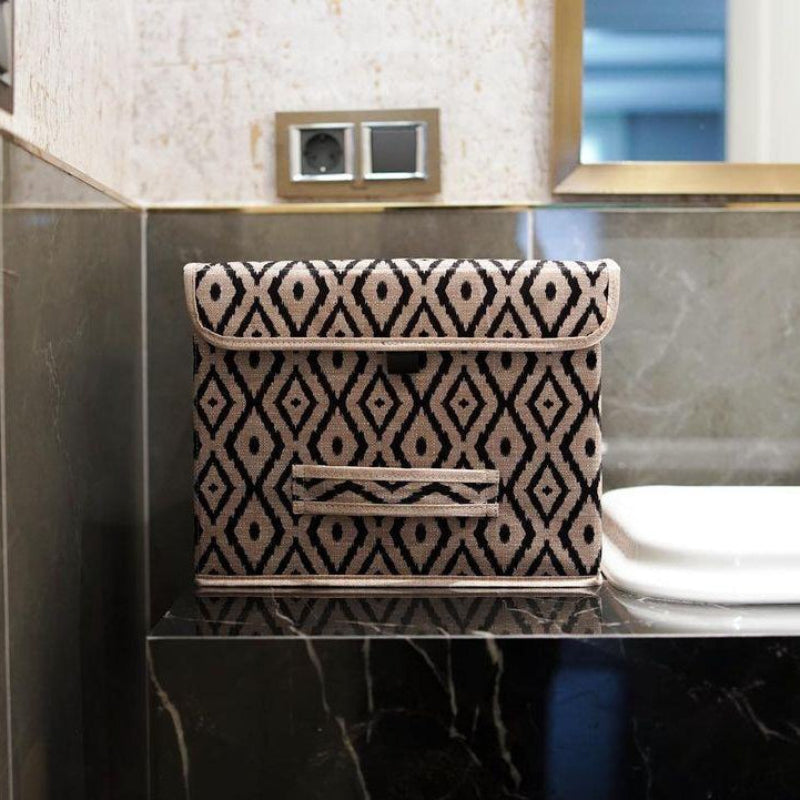Beige and black diamond-patterned fabric storage box placed on a marble bathroom counter beside a sink.