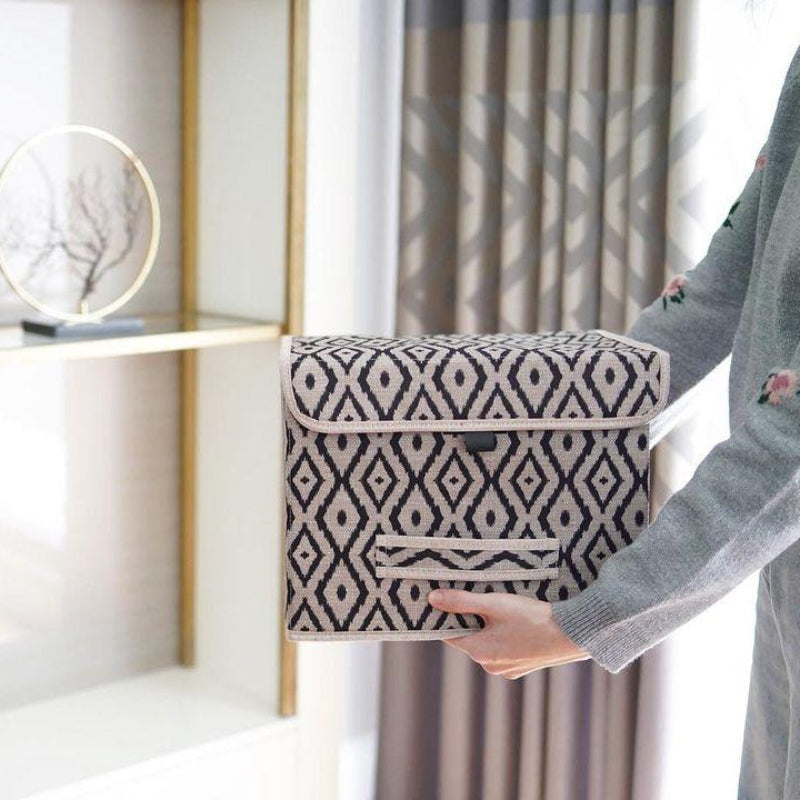 Beige and black diamond-patterned fabric storage box placed on a marble bathroom counter beside a sink.