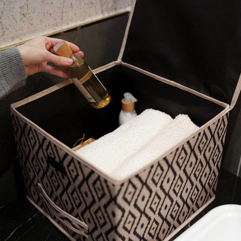Beige and black diamond-patterned fabric storage box placed on a marble bathroom counter beside a sink.