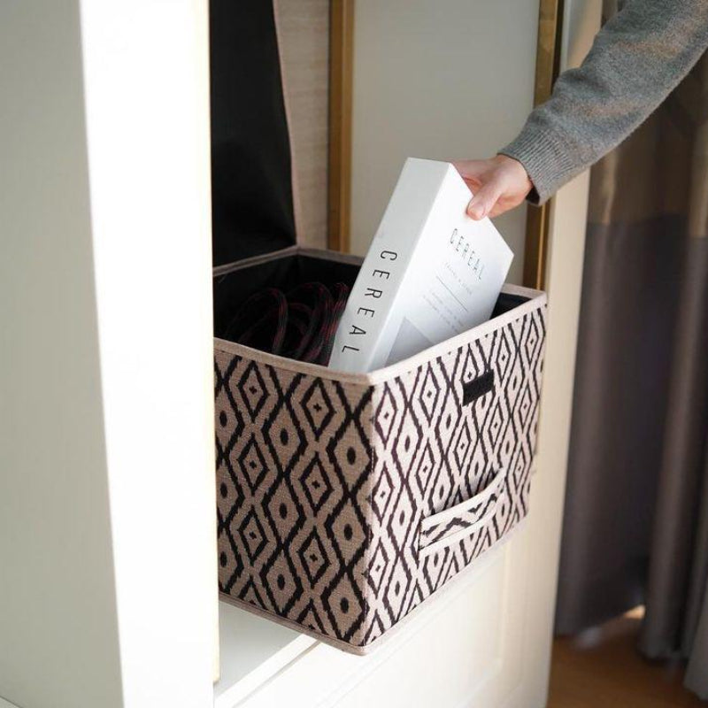 Beige and black diamond-patterned fabric storage box placed on a marble bathroom counter beside a sink.