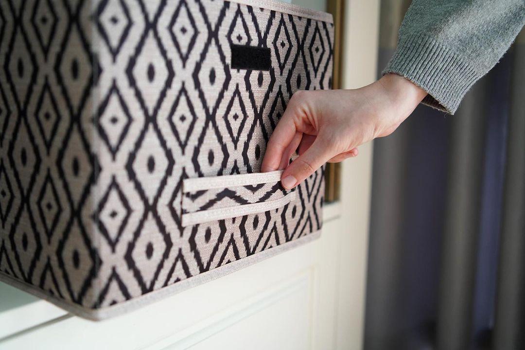Beige and black diamond-patterned fabric storage box placed on a marble bathroom counter beside a sink.