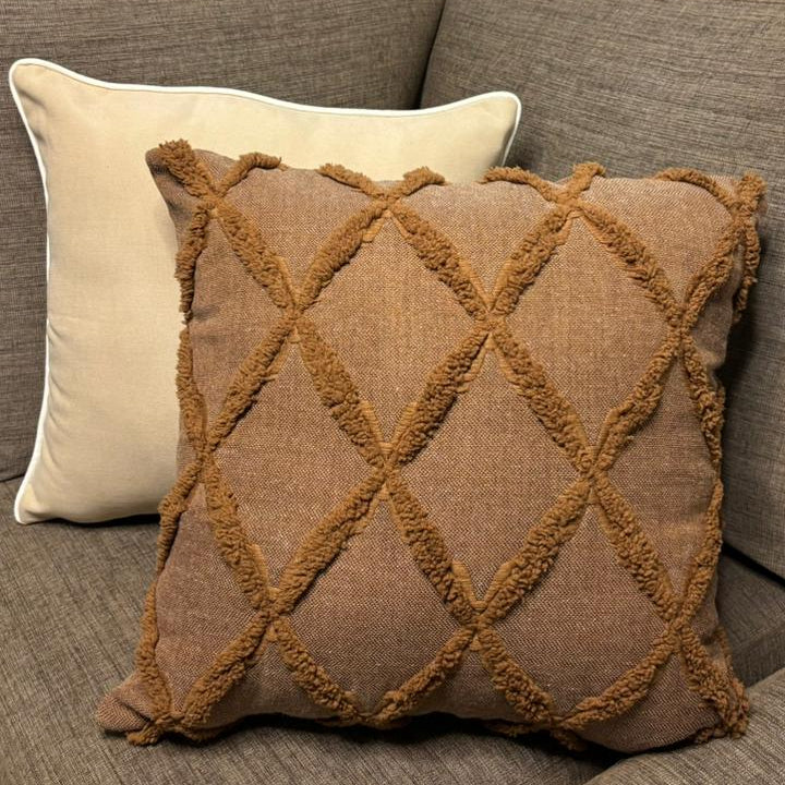 Cream cushion with white piping placed on a dark beige sofa