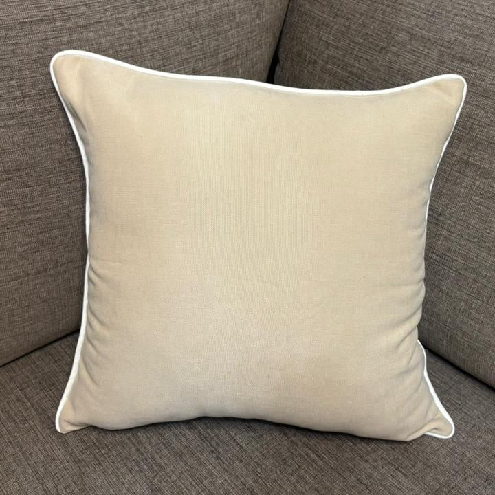 Cream cushion with white piping placed on a dark beige sofa