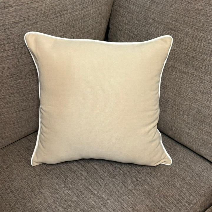 Cream cushion with white piping placed on a dark beige sofa