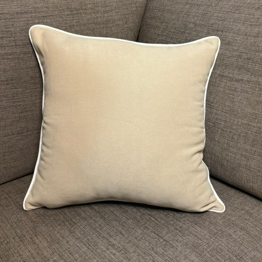 Cream cushion with white piping placed on a dark beige sofa