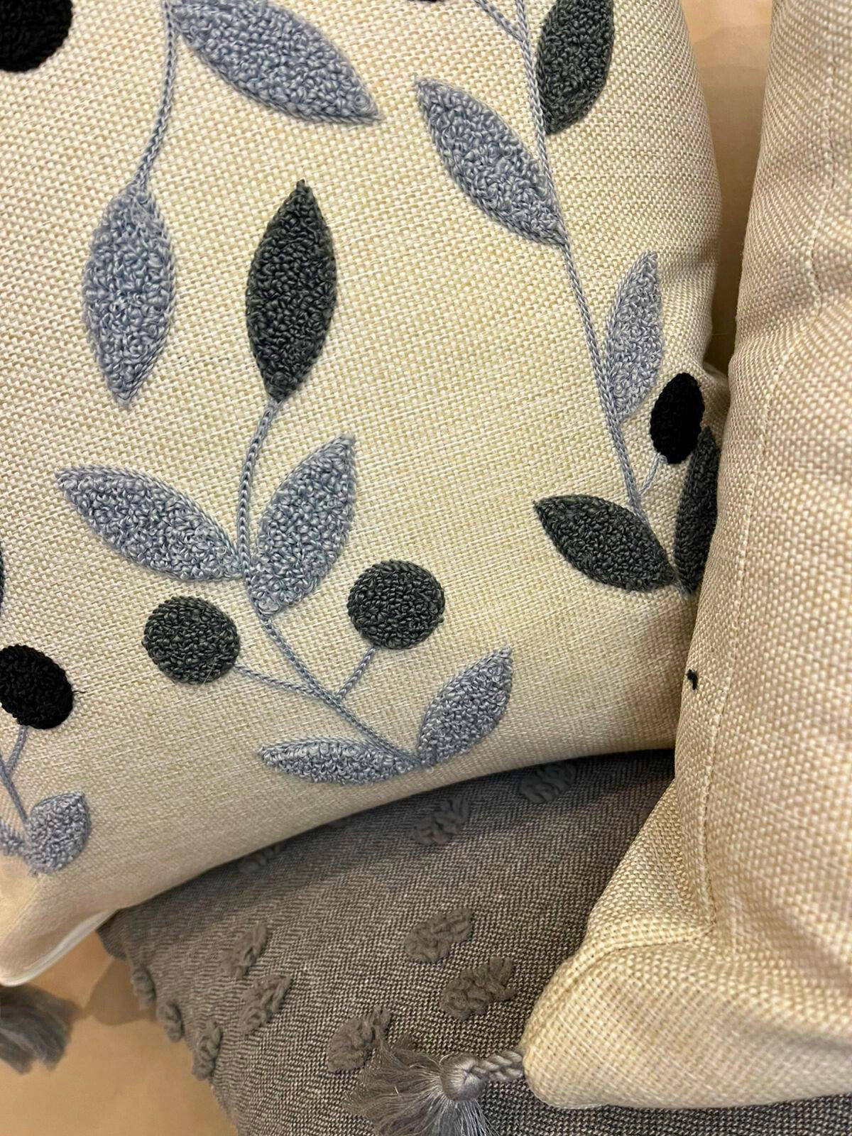 Square embroidered blue botanical cushion cover with tassels on beige sofa