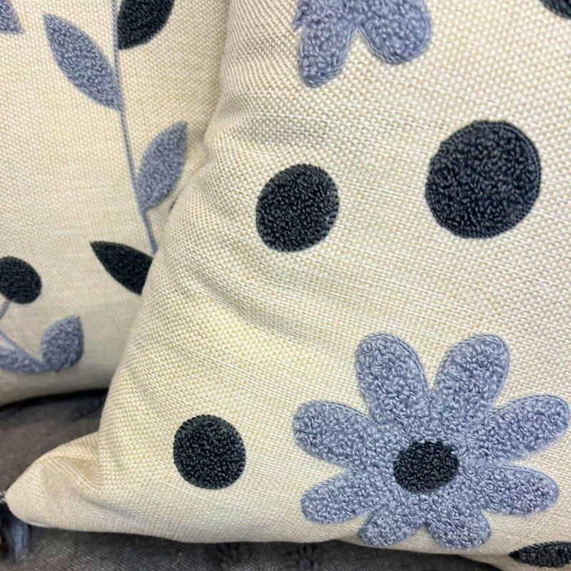 Square embroidered blue daisy cushion cover with tassels on beige sofa