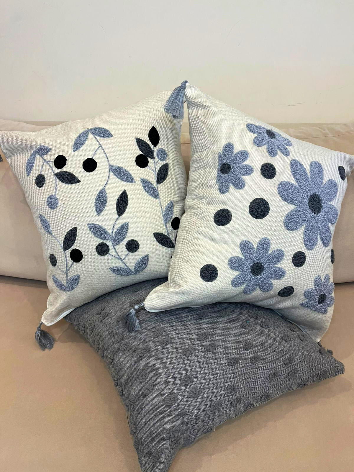 Square embroidered blue botanical cushion cover with tassels on beige sofa