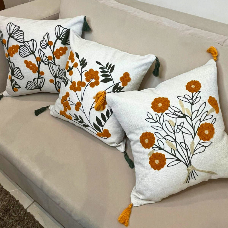 Embroidered floral cushion cover with yellow flowers, green leaves and decorative tassels on a beige sofa