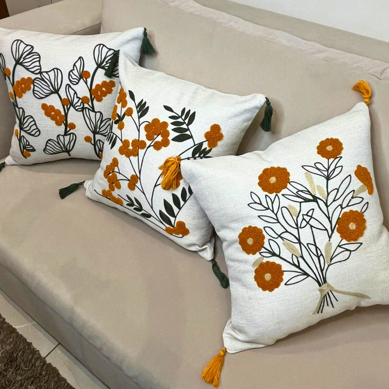 Embroidered botanical cushion cover with green leaf pattern, mustard yellow flowers and corner tassels on beige sofa