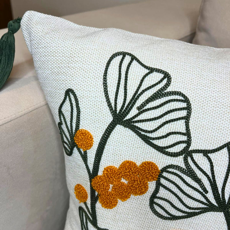 Embroidered botanical cushion cover with green leaf pattern, mustard yellow flowers and corner tassels on beige sofa