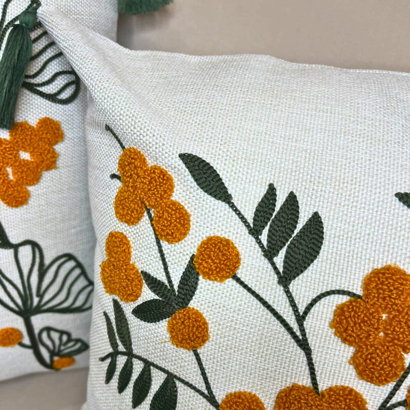 Embroidered floral cushion cover with yellow flowers, green leaves and decorative tassels on a beige sofa