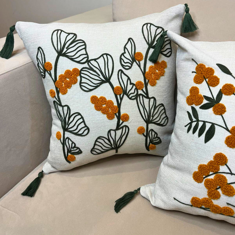 Embroidered botanical cushion cover with green leaf pattern, mustard yellow flowers and corner tassels on beige sofa