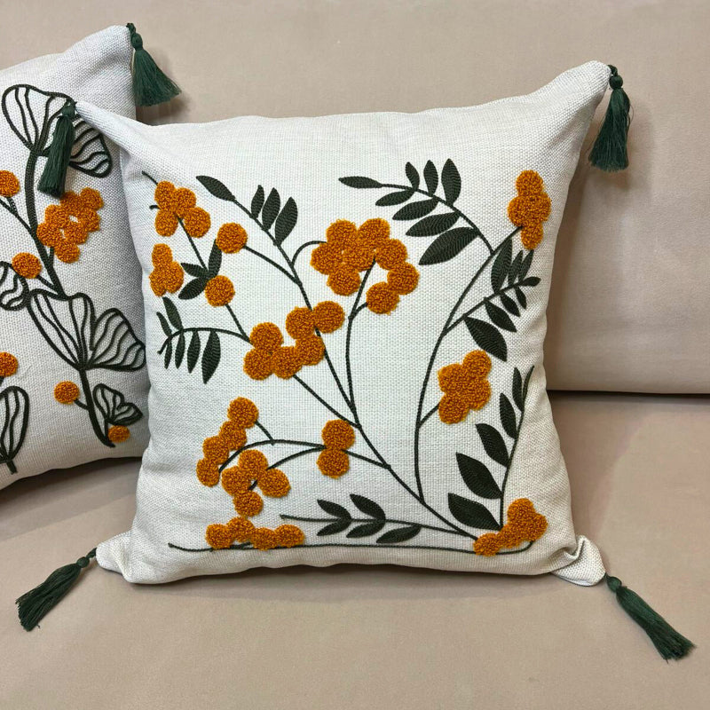 Embroidered floral cushion cover with yellow flowers, green leaves and decorative tassels on a beige sofa