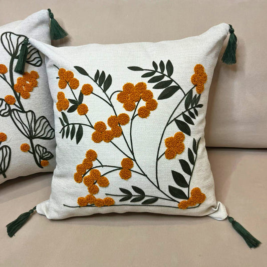 Embroidered floral cushion cover with yellow flowers, green leaves and decorative tassels on a beige sofa