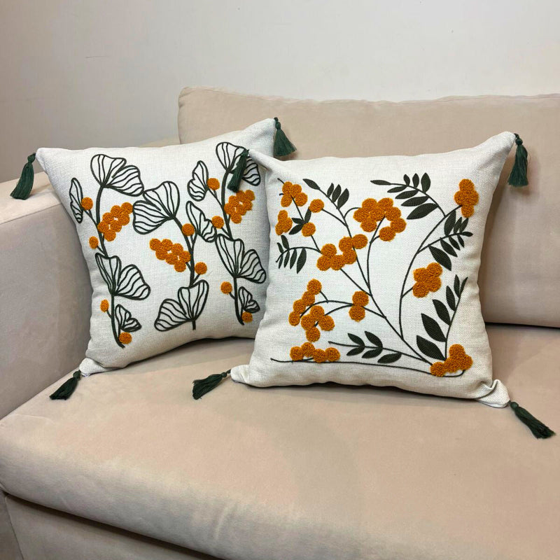 Embroidered floral cushion cover with yellow flowers, green leaves and decorative tassels on a beige sofa
