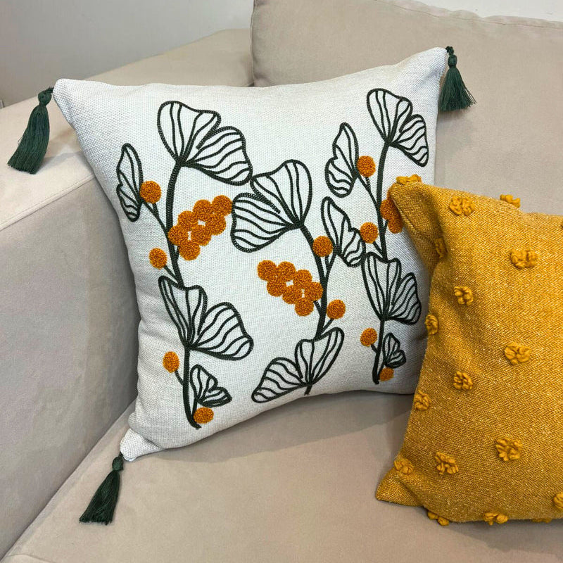 Embroidered botanical cushion cover with green leaf pattern, mustard yellow flowers and corner tassels on beige sofa