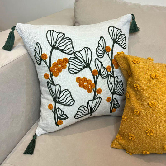 Embroidered botanical cushion cover with green leaf pattern, mustard yellow flowers and corner tassels on beige sofa