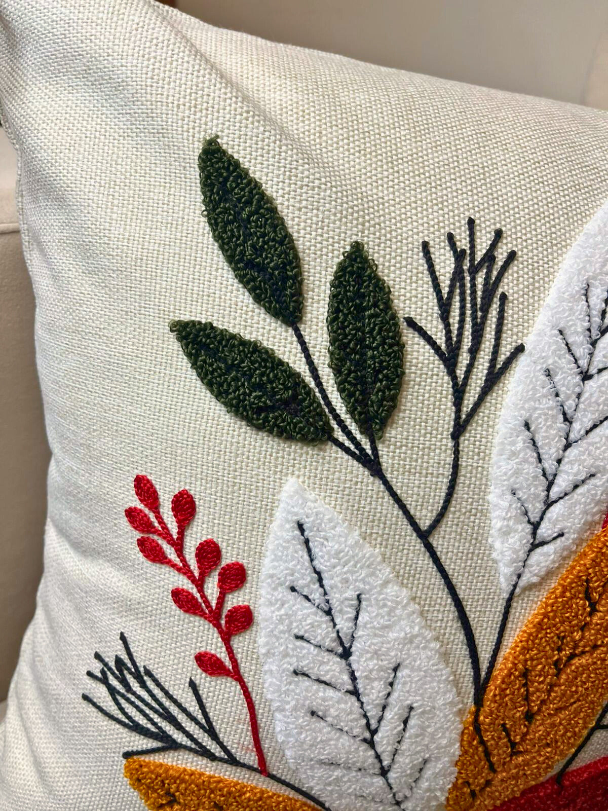 Square embroidered cushion cover with multicolor leaf design and tassels on sofa