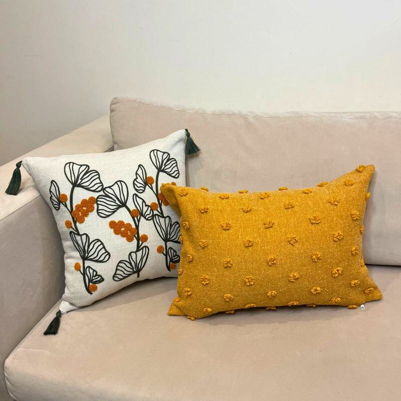 Embroidered botanical cushion cover with green leaf pattern, mustard yellow flowers and corner tassels on beige sofa