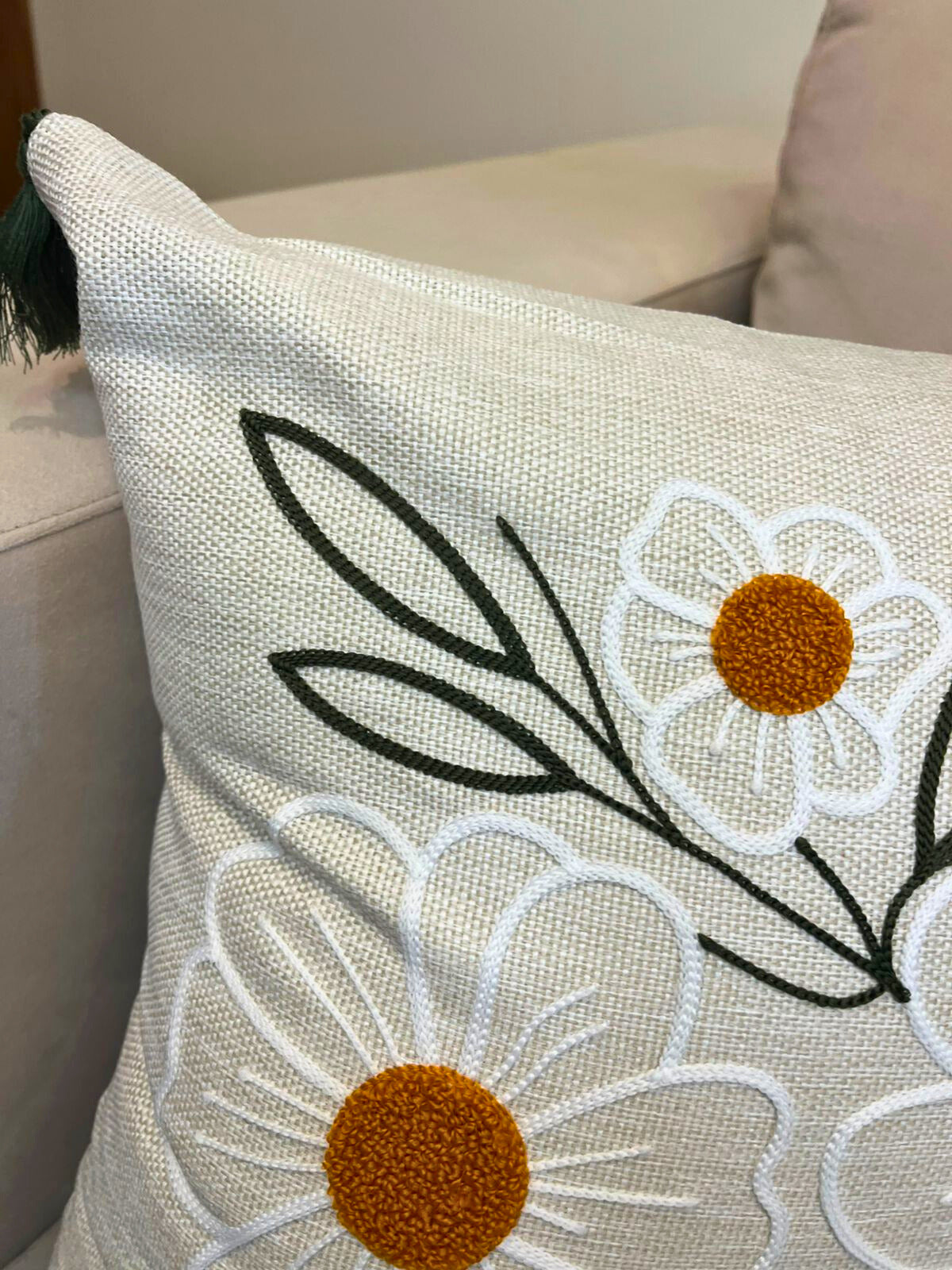 Square embroidered daisy cushion cover with tassels on beige sofa