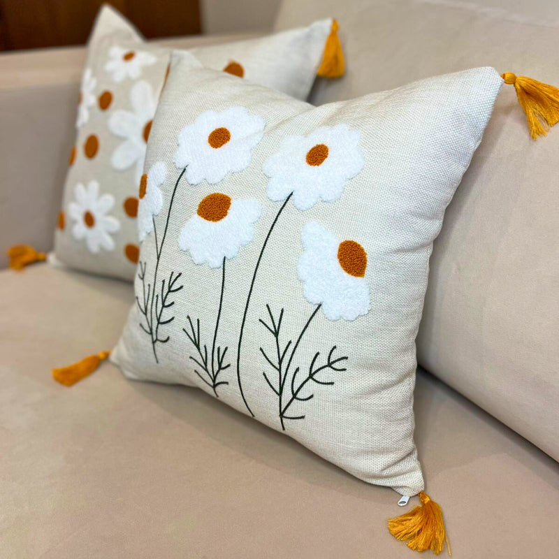 Square embroidered daisy cushion cover with tassels and white floral design on beige sofa
