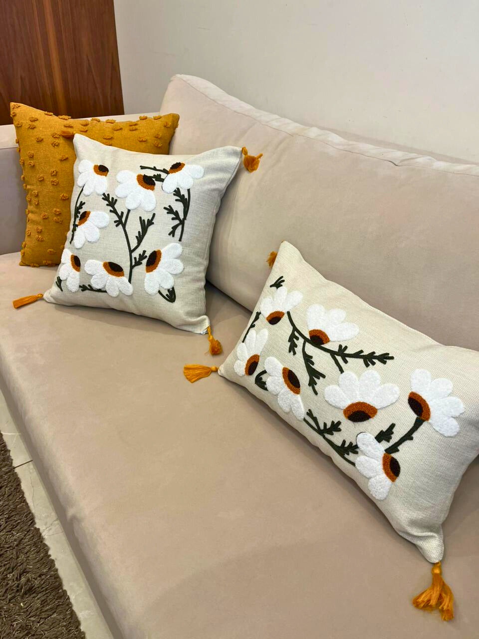 Square embroidered daisy cushion cover with tassels on beige sofa
