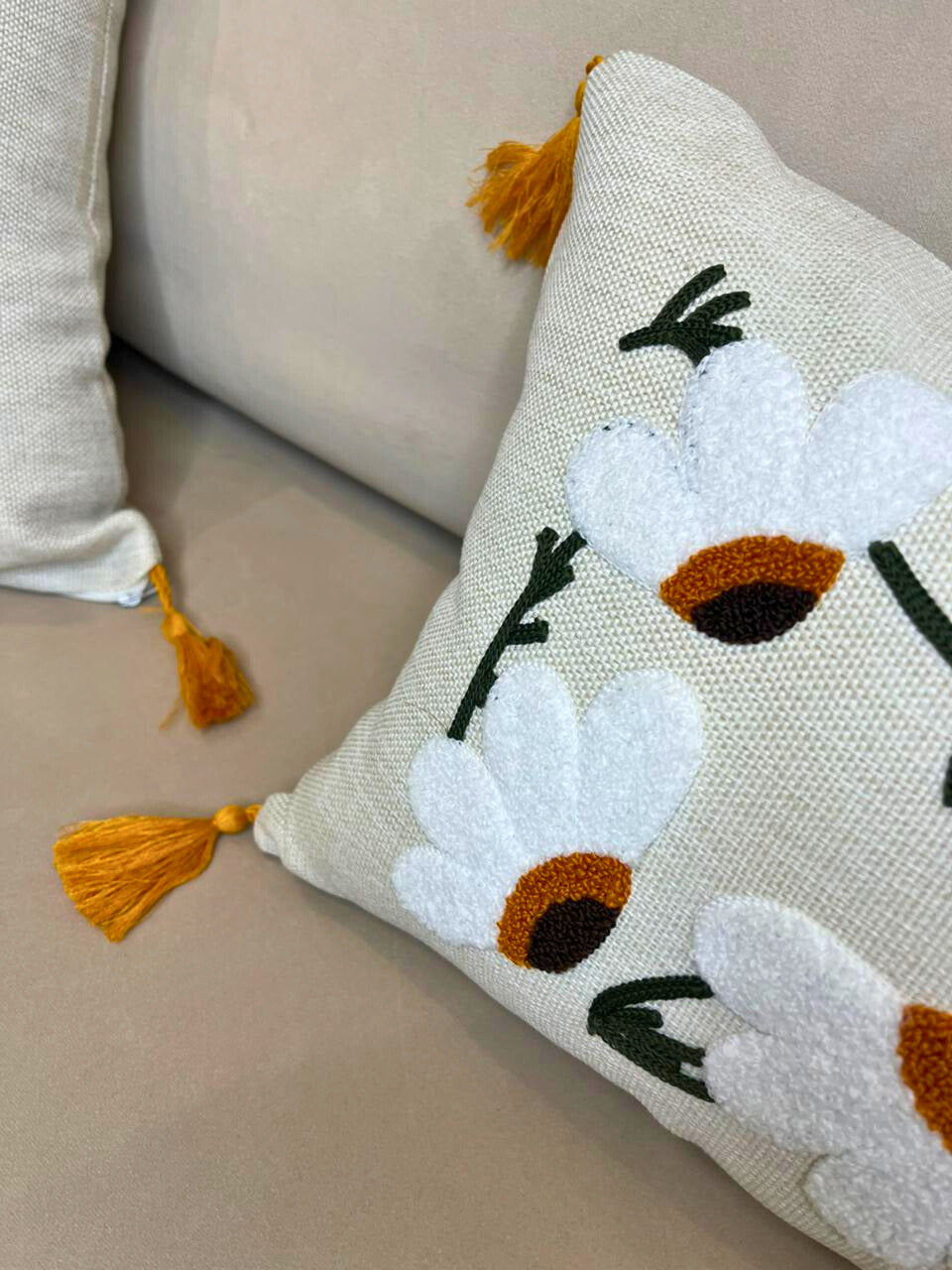 Rectangular embroidered daisy cushion cover with tassels on beige sofa